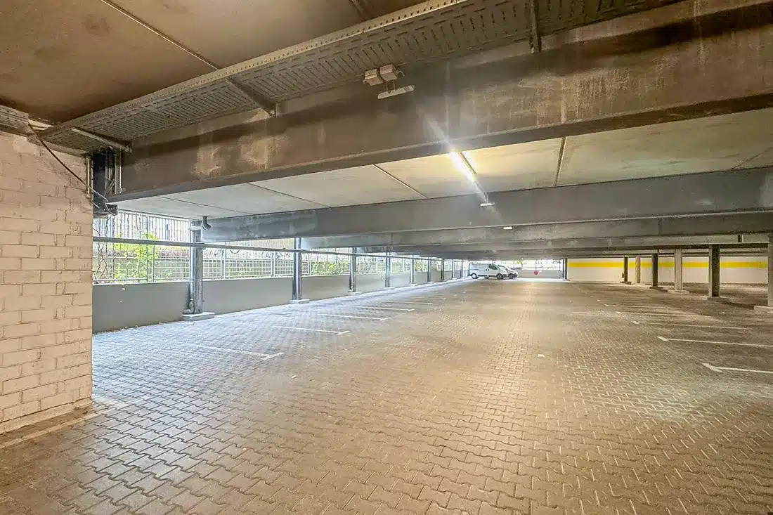 Innenansicht eines leerstehenden Parkhauses mit Verbundsteinpflaster und massiven Stahlbetonträgern vor der Sanierung durch Resintech.