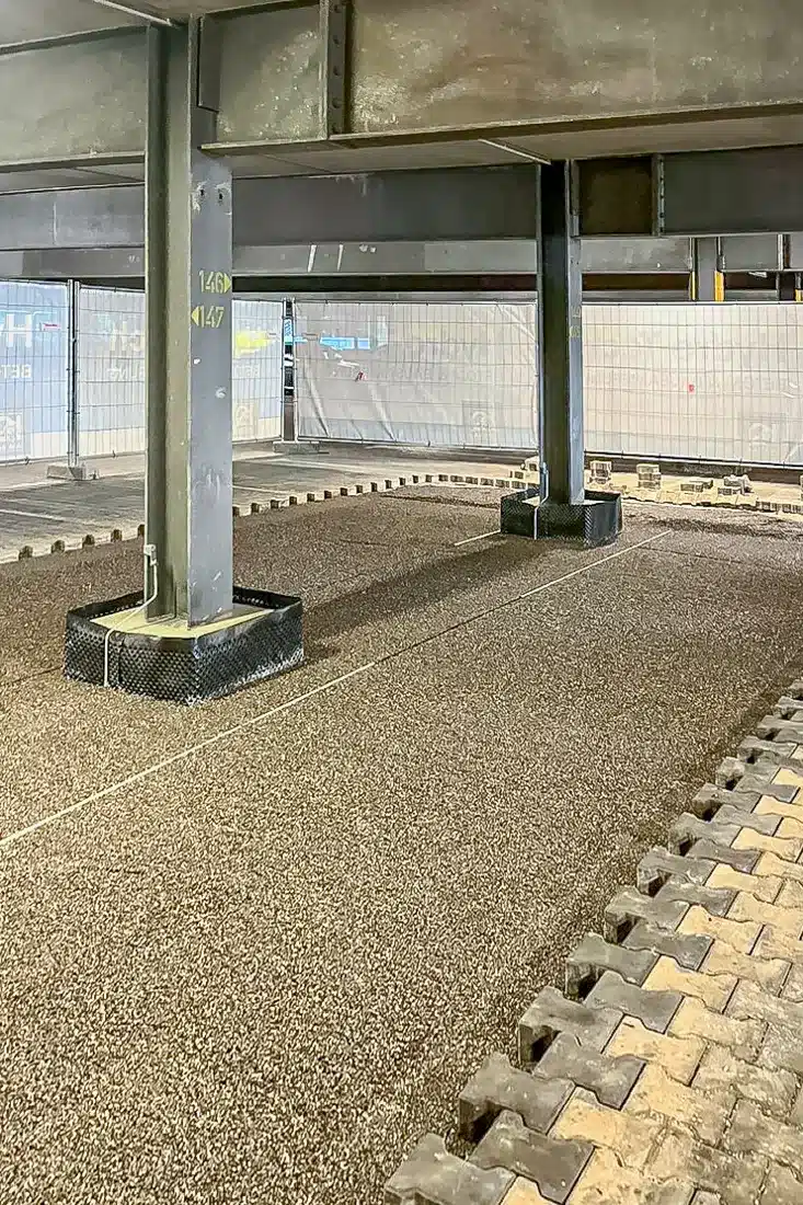 Vorbereitete Fläche mit Schüttgut und abgedichteten Stützensockeln für den neuen Bodenaufbau in einem Parkhaus.