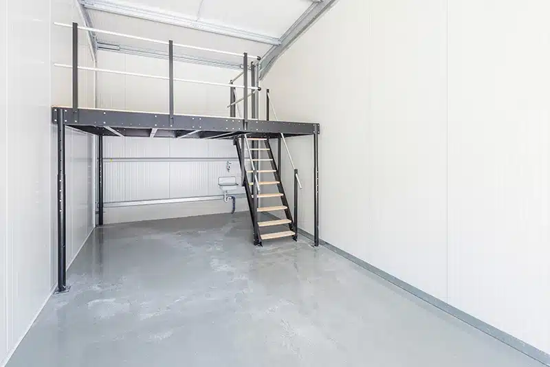 Ein Lagerraum mit einer kleinen Galerie und Treppe. Der Fußboden aus Beton ist frisch beschichtet und die Innenwände sauber in weiß gestrichen.