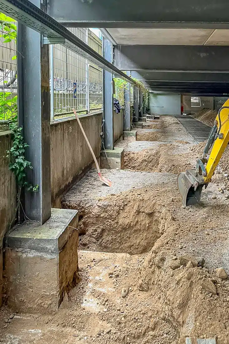 Tiefbauarbeiten im Parkhaus: Ausgehobene Gruben entlang der Außenwand zur Verstärkung der Fundamente durch Resintech Augsburg.