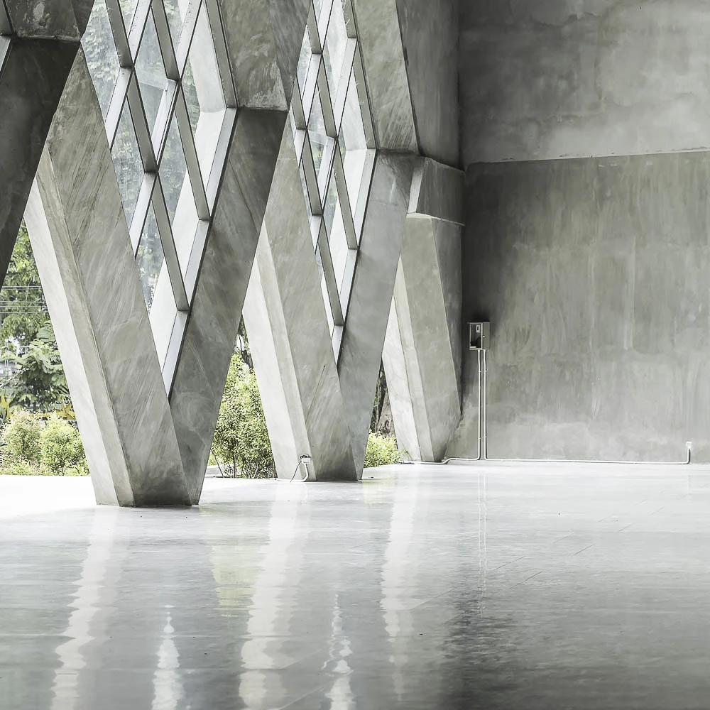 Minimalistische Architektur: Sichtbetonwände kombiniert mit einer spiegelnden, hellen Bodenveredelung in einer Galerie.